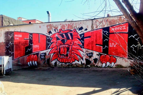 Lettrages et personnage rouge sur mur par le graffeur Fuzi
